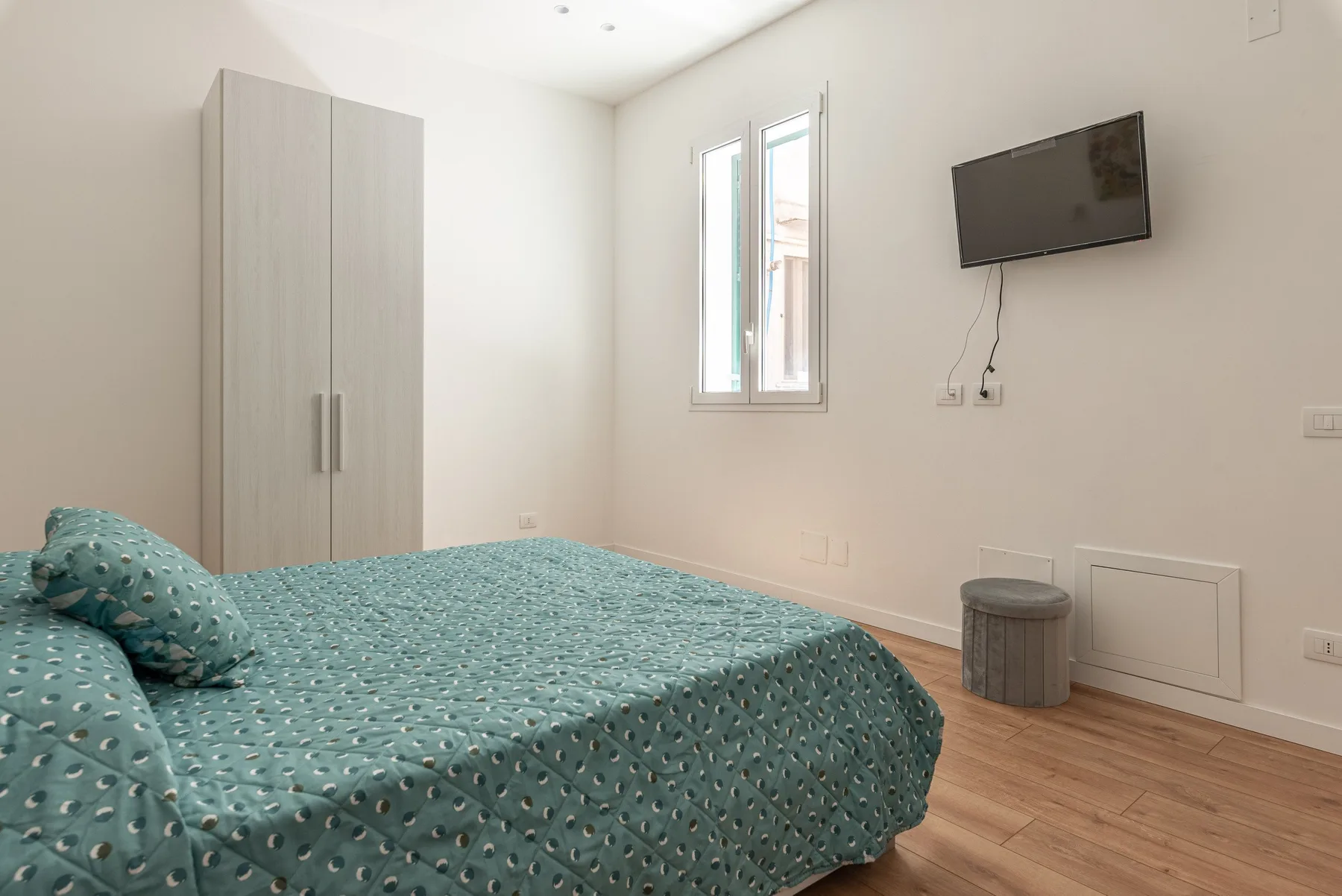 Un dormitorio con una cama, un armario y un televisor en la pared.