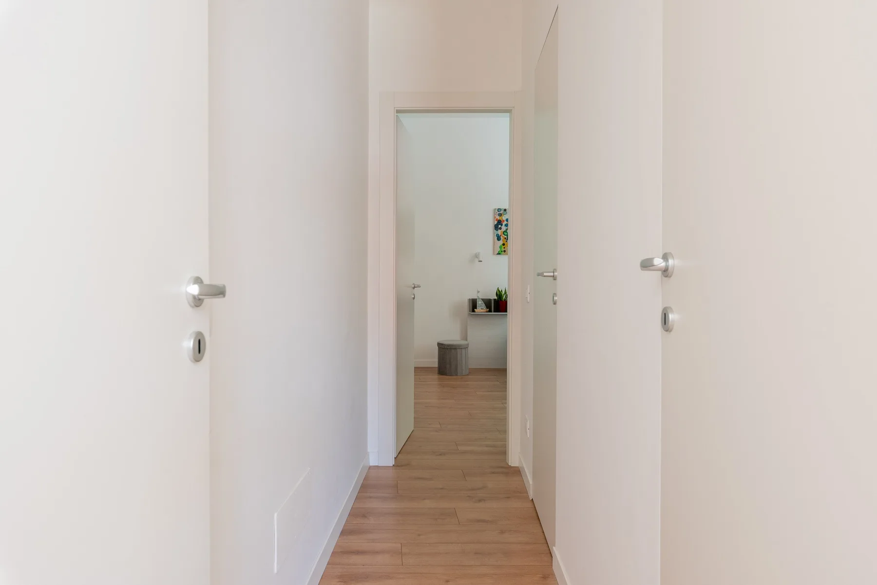 Un pasillo luminoso con suelo de madera y una puerta abierta al fondo.