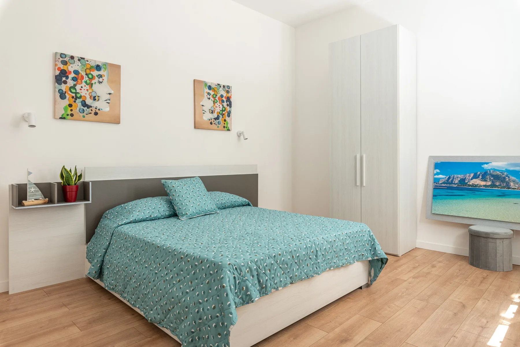 Un dormitorio con una cama cubierta de ropa de cama turquesa y arte colorido en la pared.