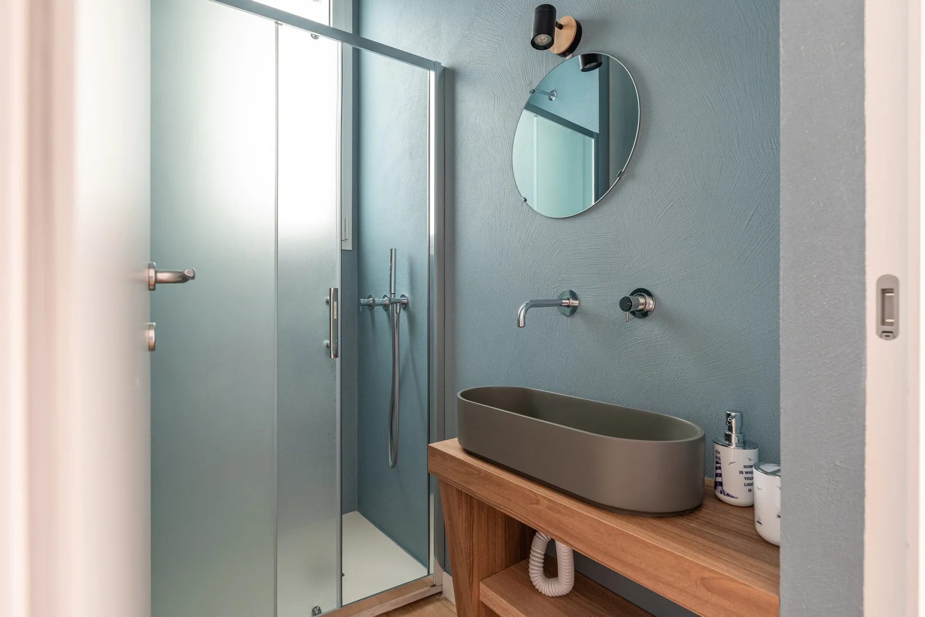 Un baño moderno con ducha de vidrio, espejo redondo y mueble de madera.