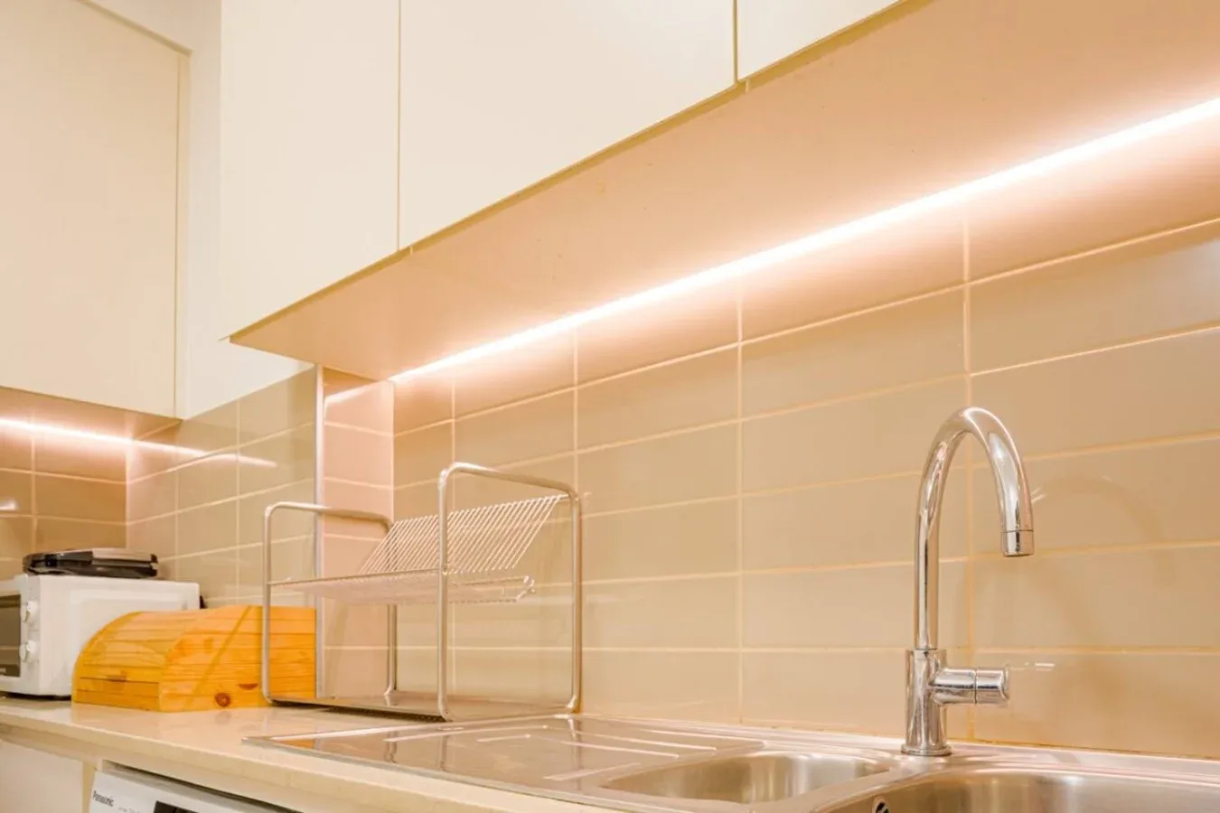 A modern kitchen with a stainless-steel sink beneath warm cabinet lighting.