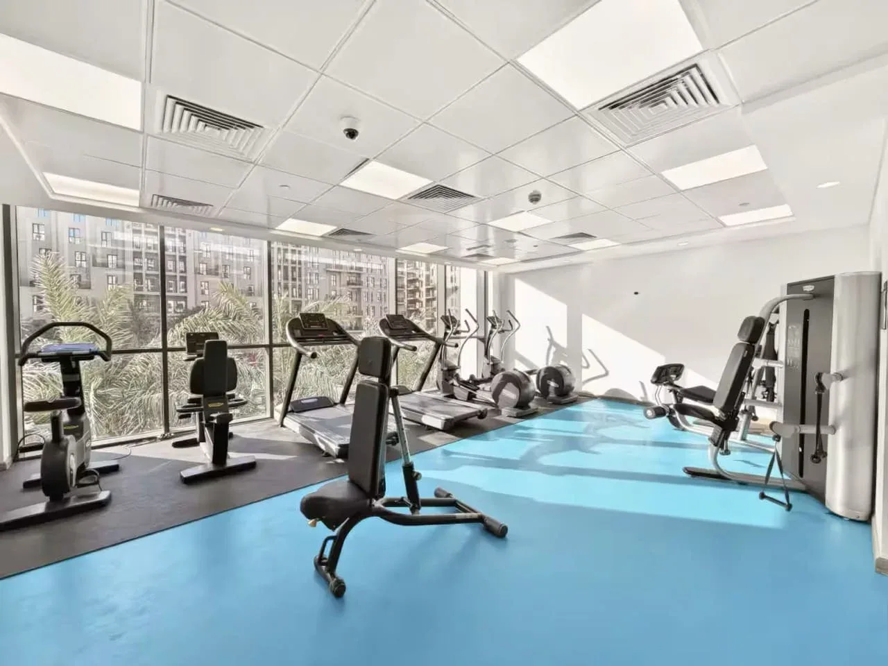 A bright fitness room with exercise machines arranged beside large windows.