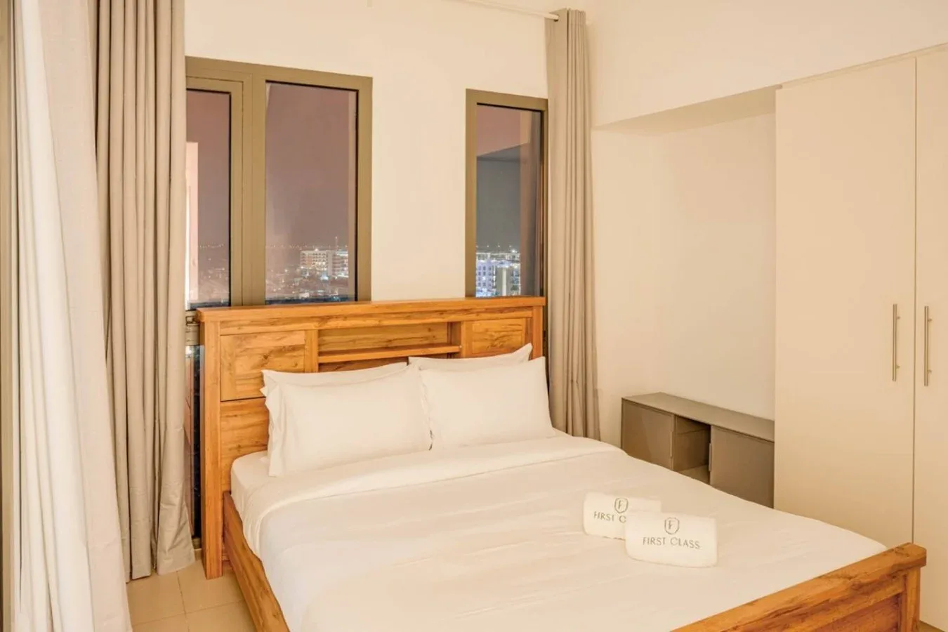 A bedroom with a bed, wooden headboard, and curtained windows.