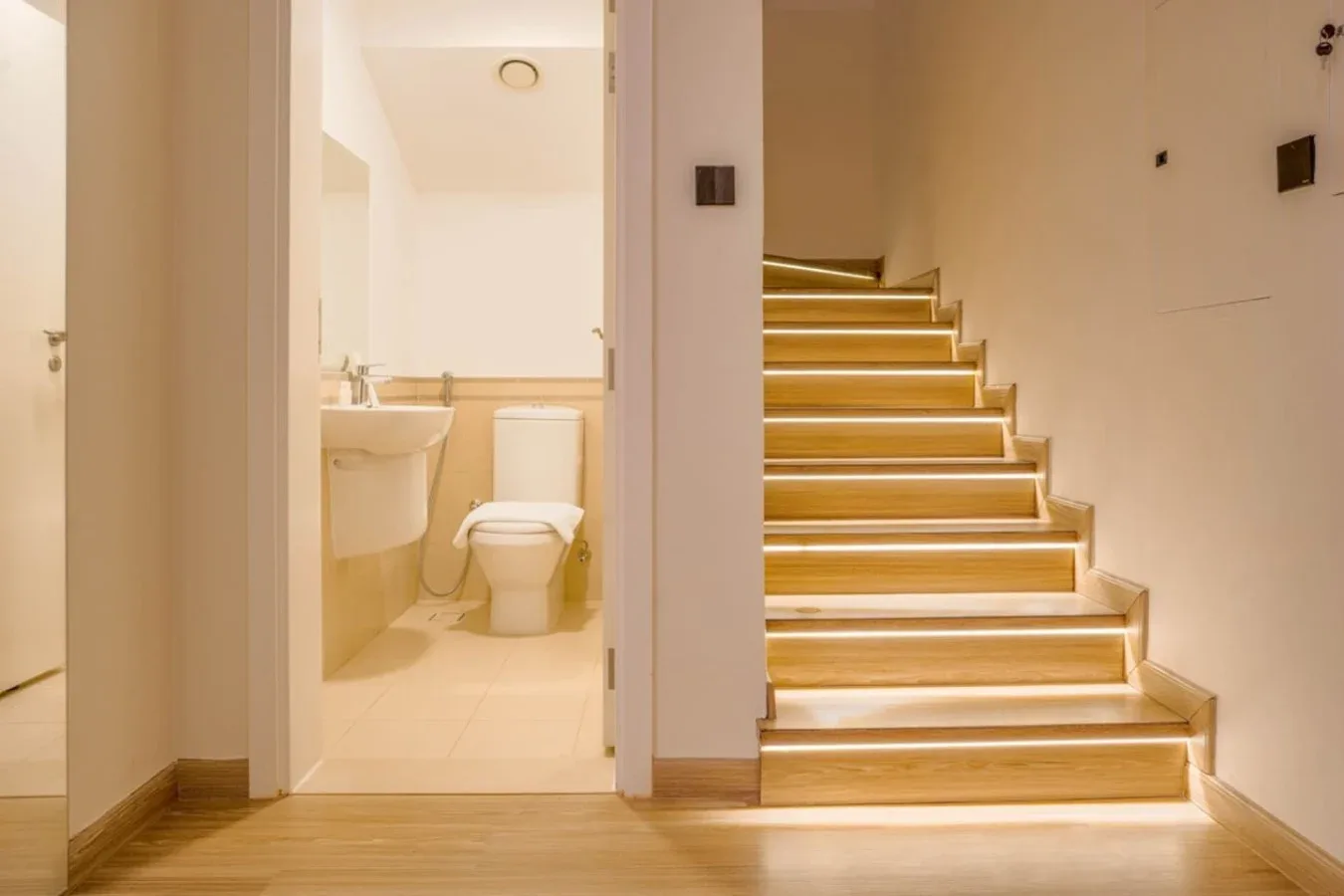 A brightly lit interior hallway with a staircase beside an open bathroom doorway.