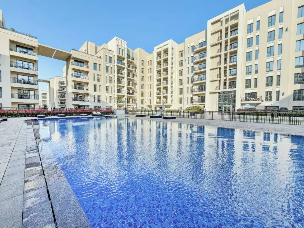 A large outdoor swimming pool sits in front of modern multi-story buildings.