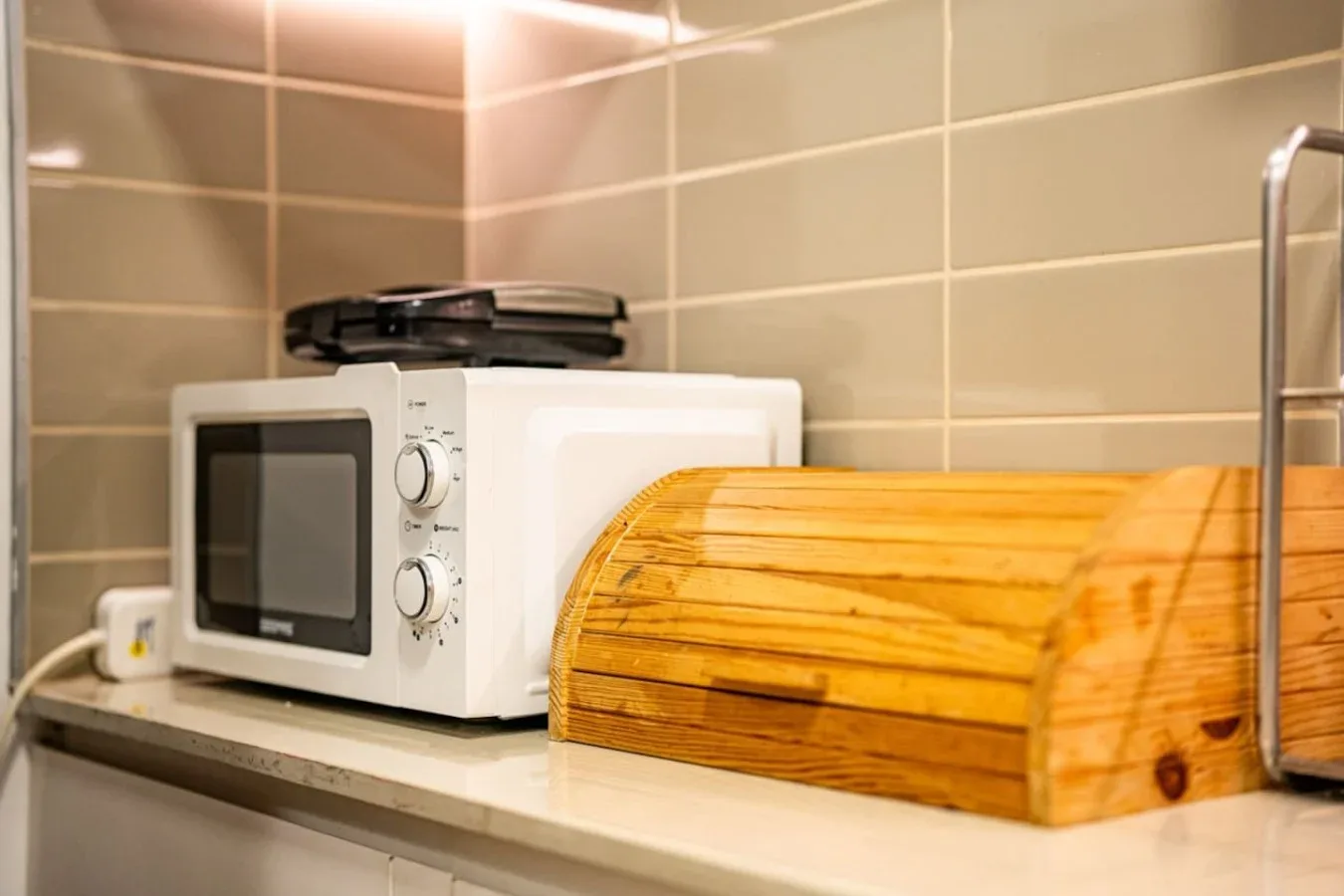 A tiled kitchen counter with a microwave and a wooden bread box.