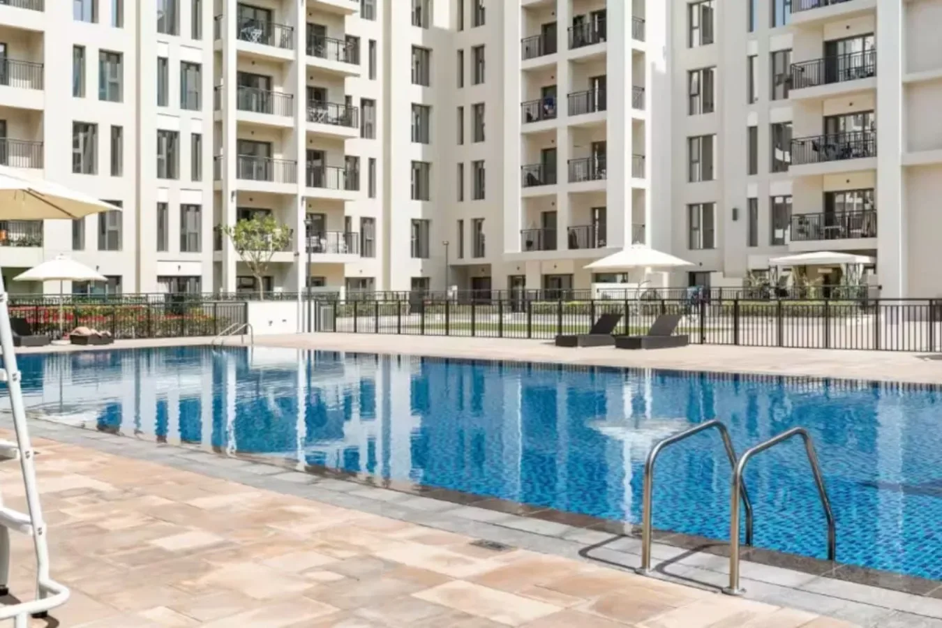 Una piscina al aire libre está junto a una terraza pavimentada y edificios de apartamentos.