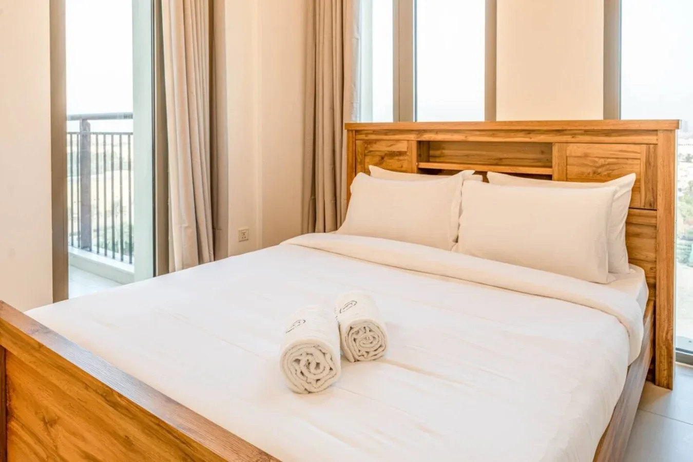 A bedroom with a wooden bed, white bedding, and rolled towels.