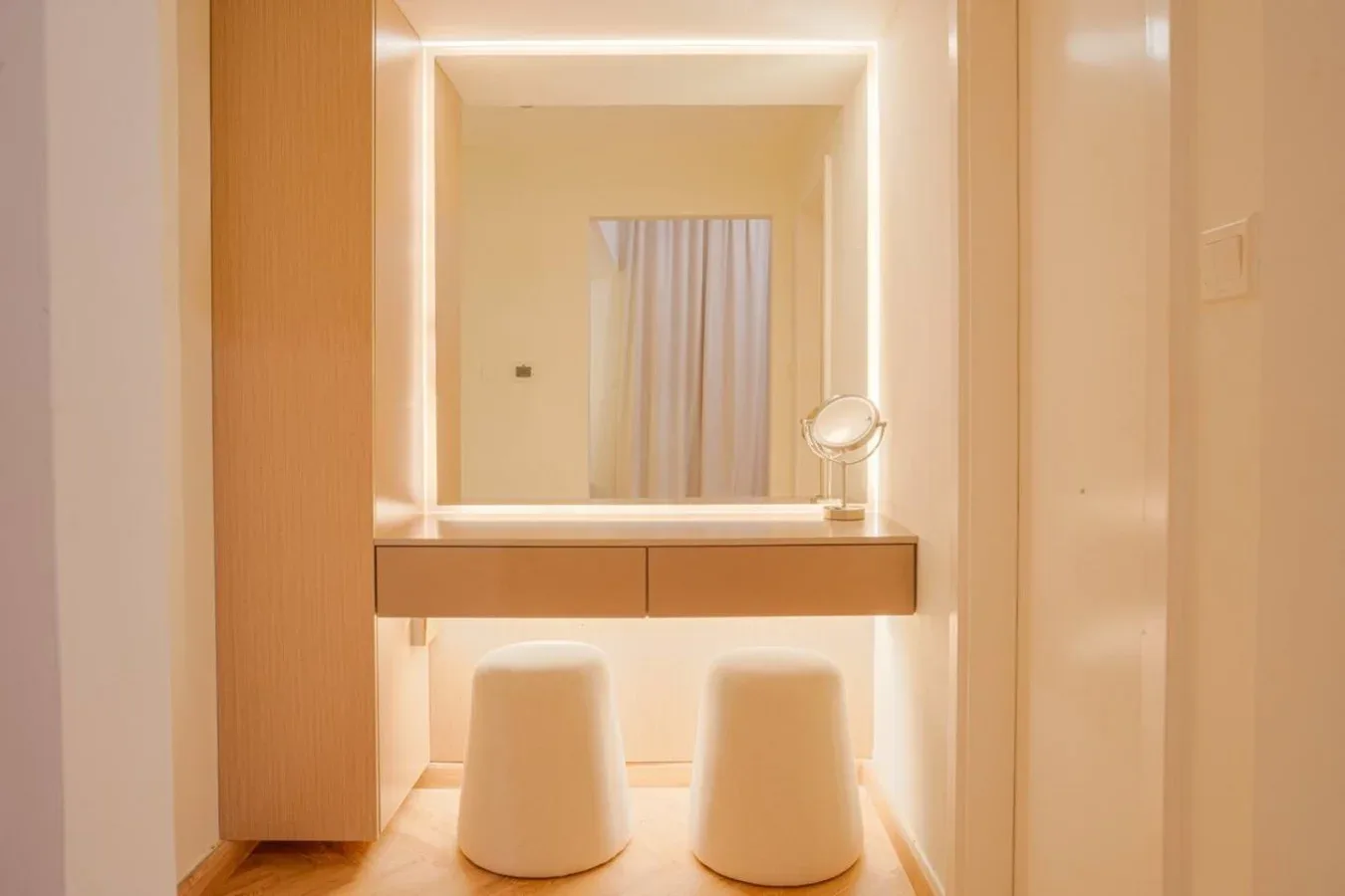 A vanity area with an illuminated mirror and two stools.