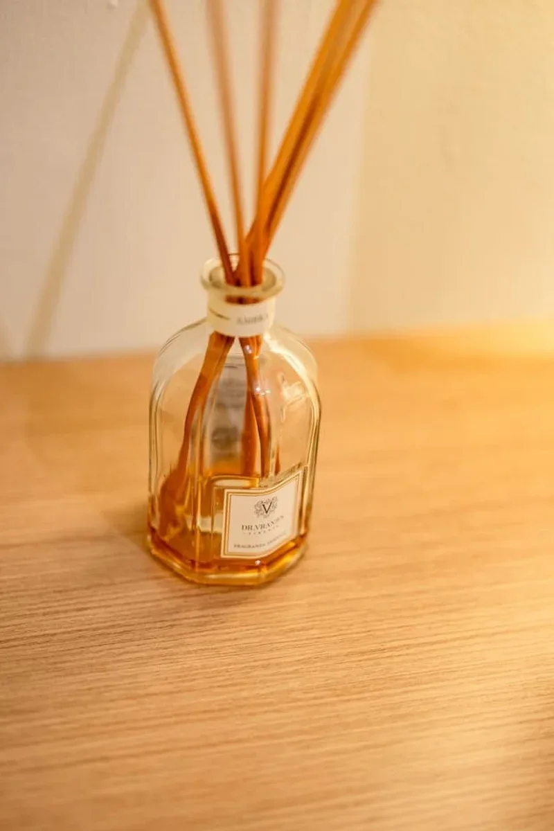 An amber glass reed diffuser sits on a light wooden surface.