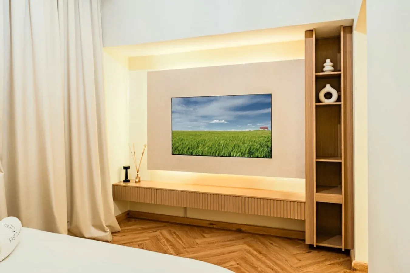 A bedroom features a wall-mounted television above a low built-in cabinet.