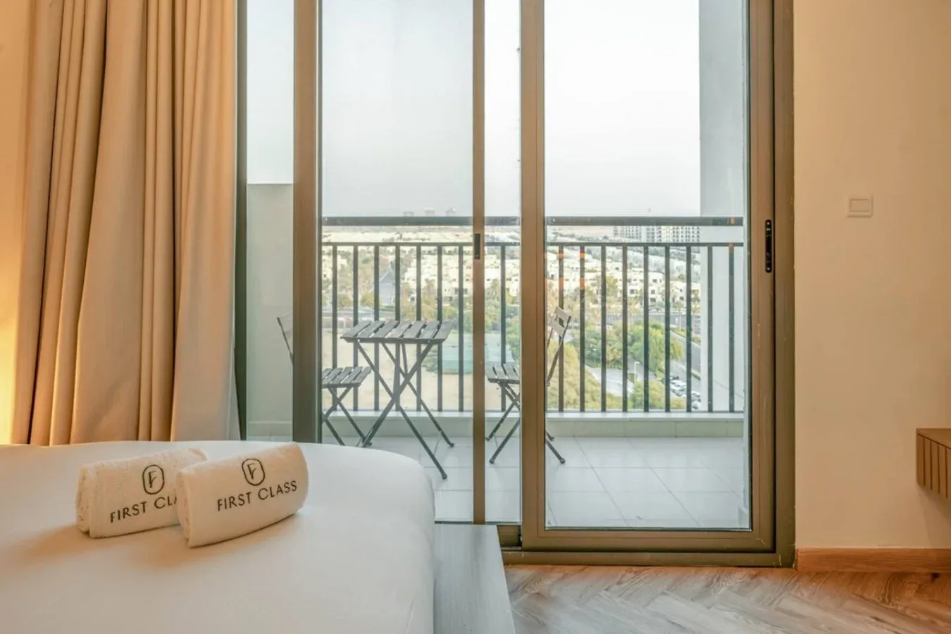A bedroom opens onto a balcony with small outdoor seating and a city view.