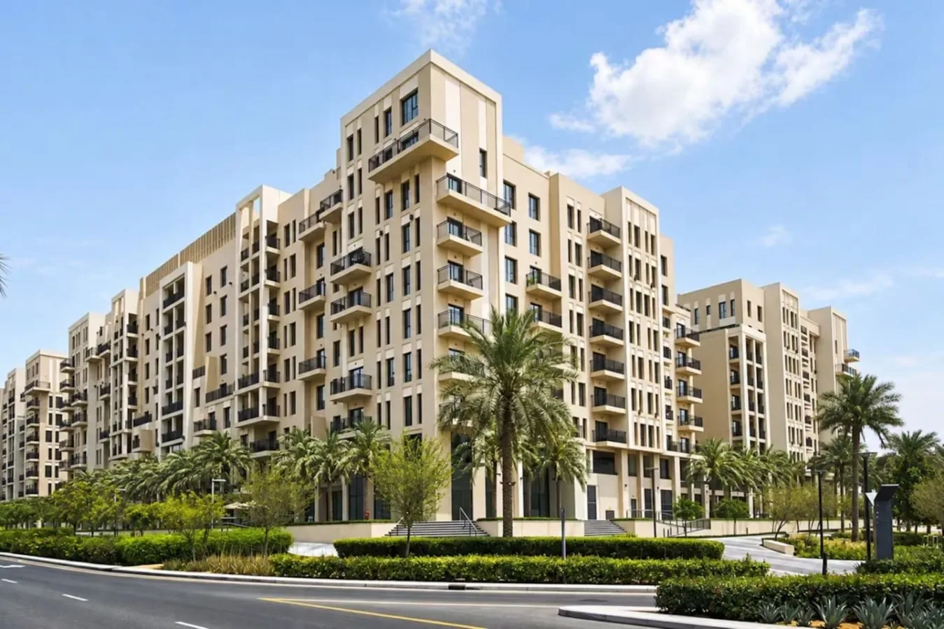 A modern apartment building stands behind landscaped grounds and palm trees.