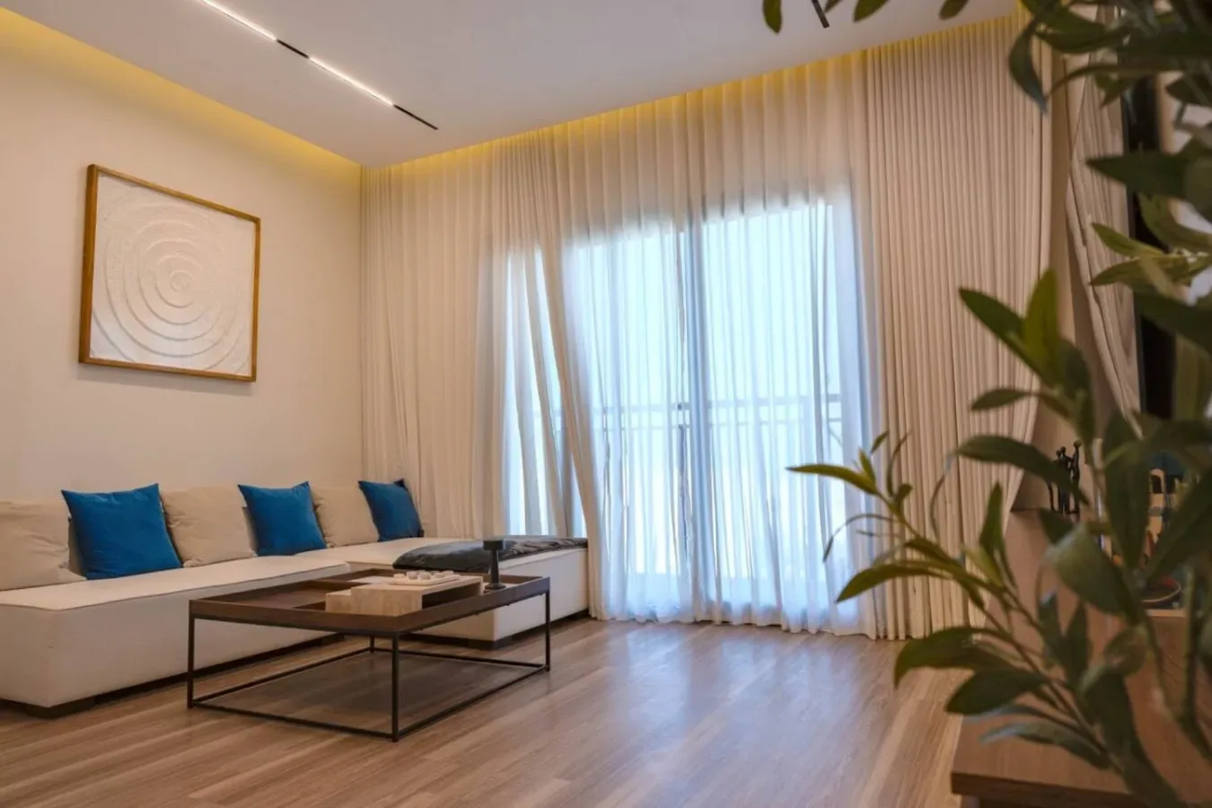 A living room with seating, a coffee table, and sheer curtains over a bright window.