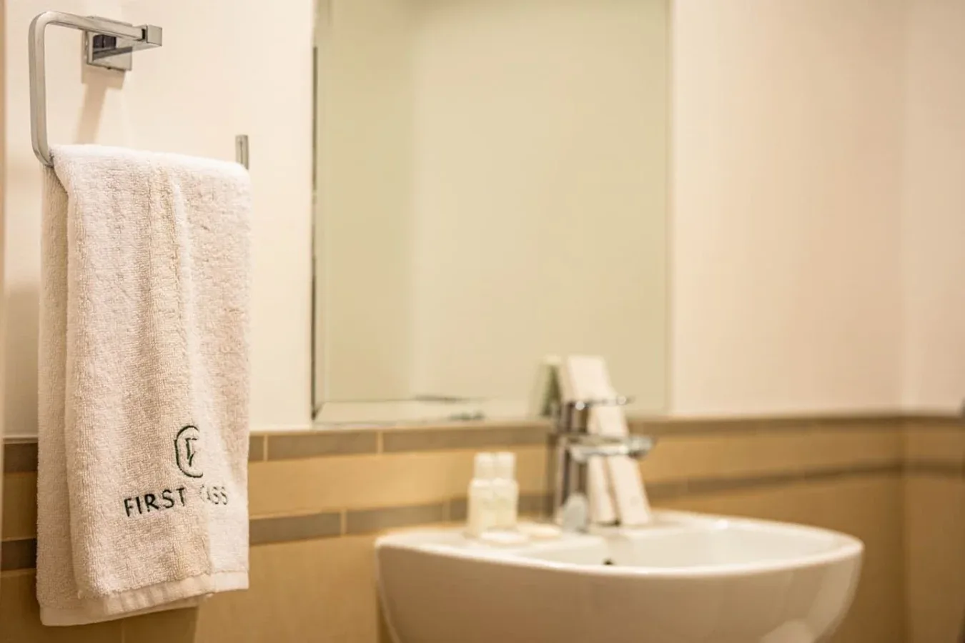 A bathroom sink sits beneath a mirror, with a towel hanging nearby.
