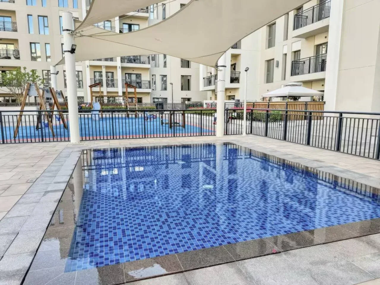An outdoor swimming pool sits beneath a shade canopy in an apartment courtyard.