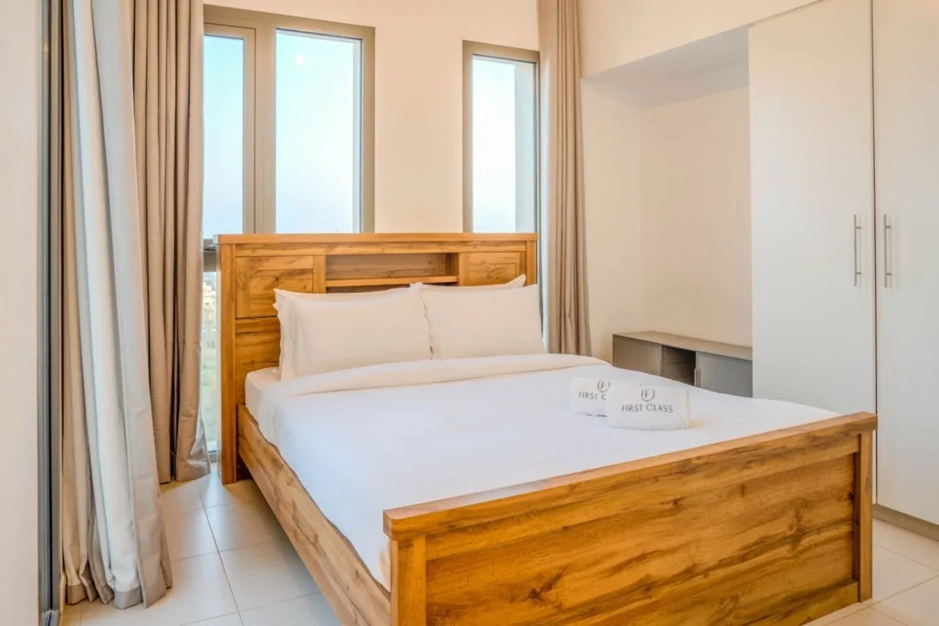 A bedroom with a wooden bed, white bedding, and tall windows.