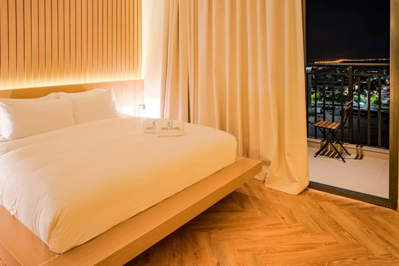 A bedroom with a bed beside curtains opening onto a balcony at night.