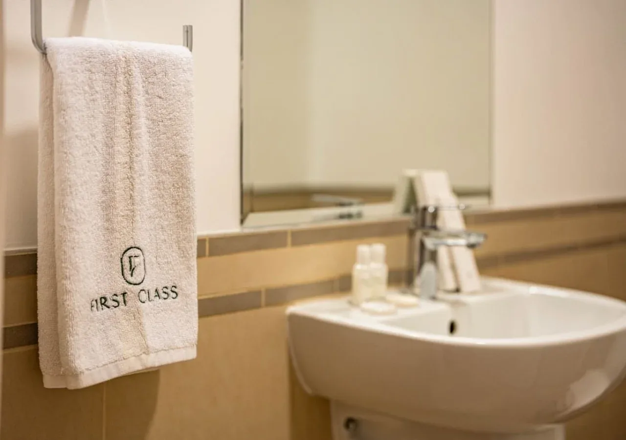 A bathroom sink sits beneath a mirror, with a towel hanging nearby.