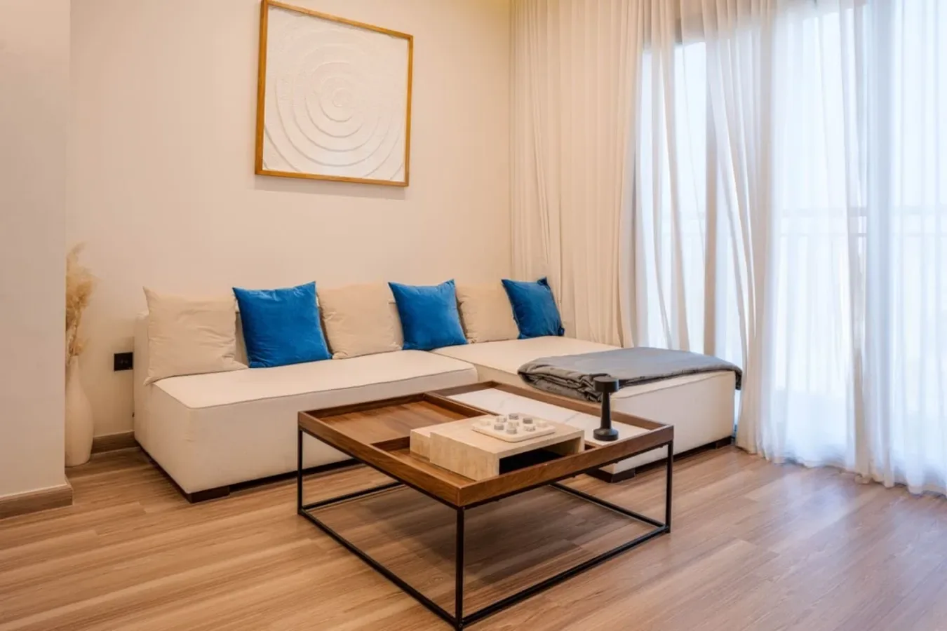 Una sala luminosa con un sofá seccional, una mesa de centro y cortinas translúcidas.