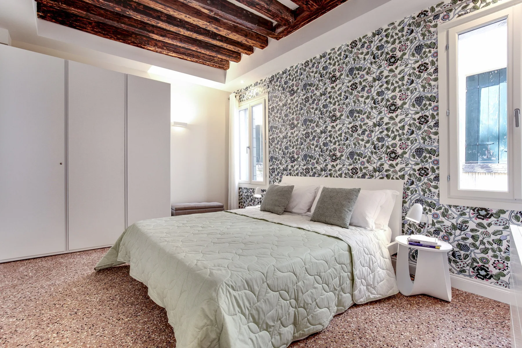 A bedroom with a bed against a patterned floral wall.