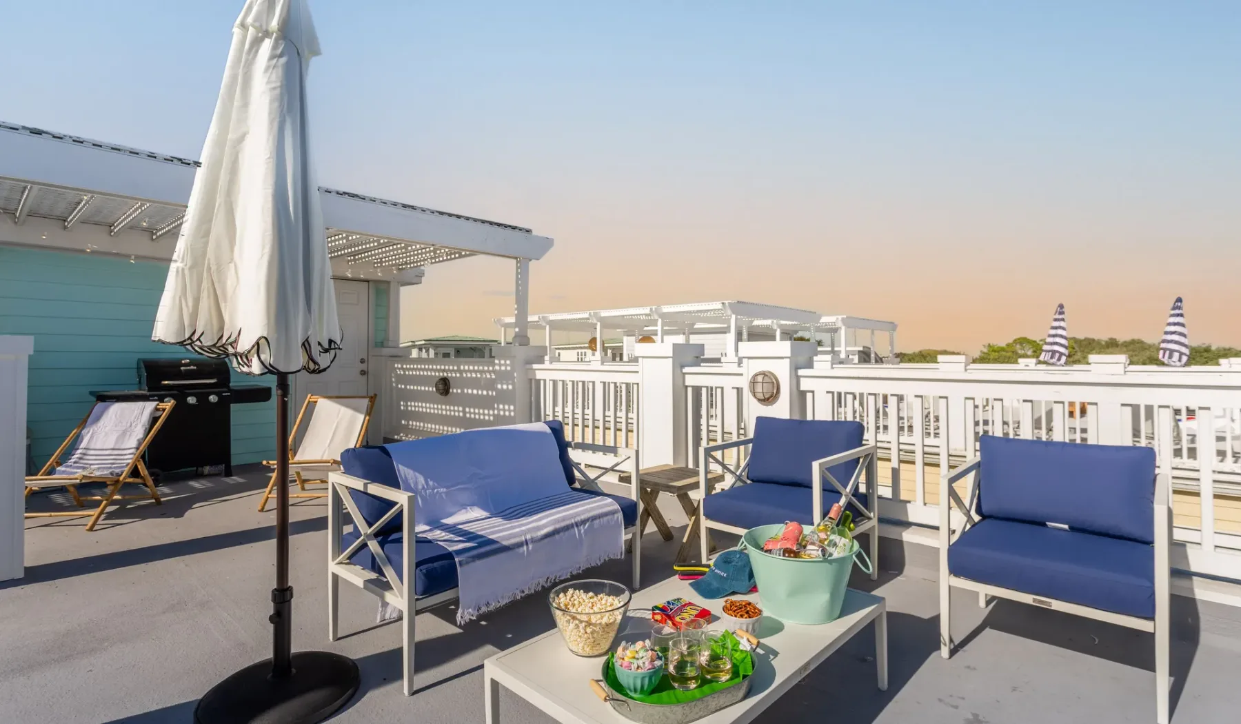 A rooftop patio has blue seating, a table, and a closed umbrella.