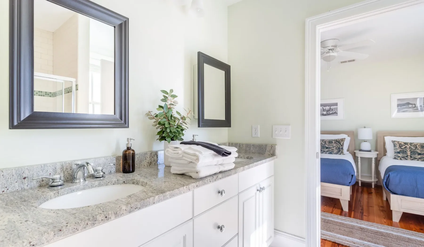 A bathroom vanity with a sink and mirror opens onto a bedroom.