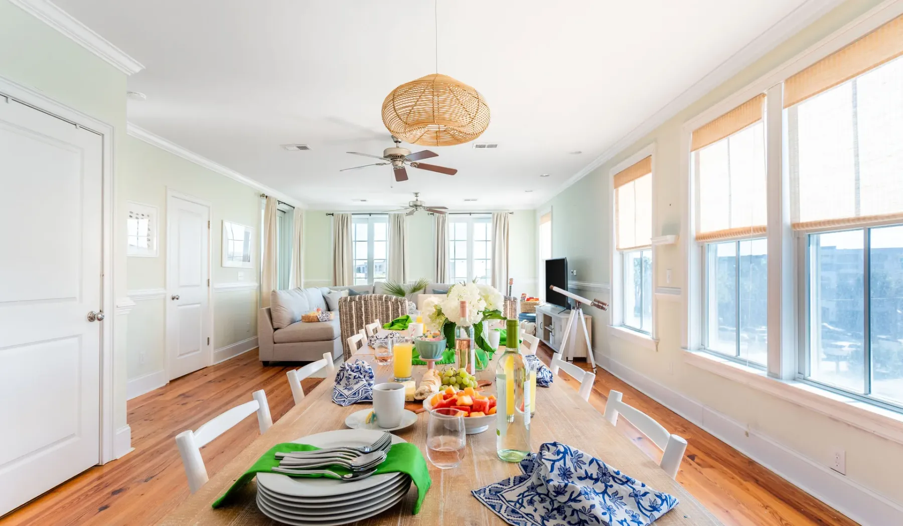 A bright dining room with a long table set for a meal beside large windows.