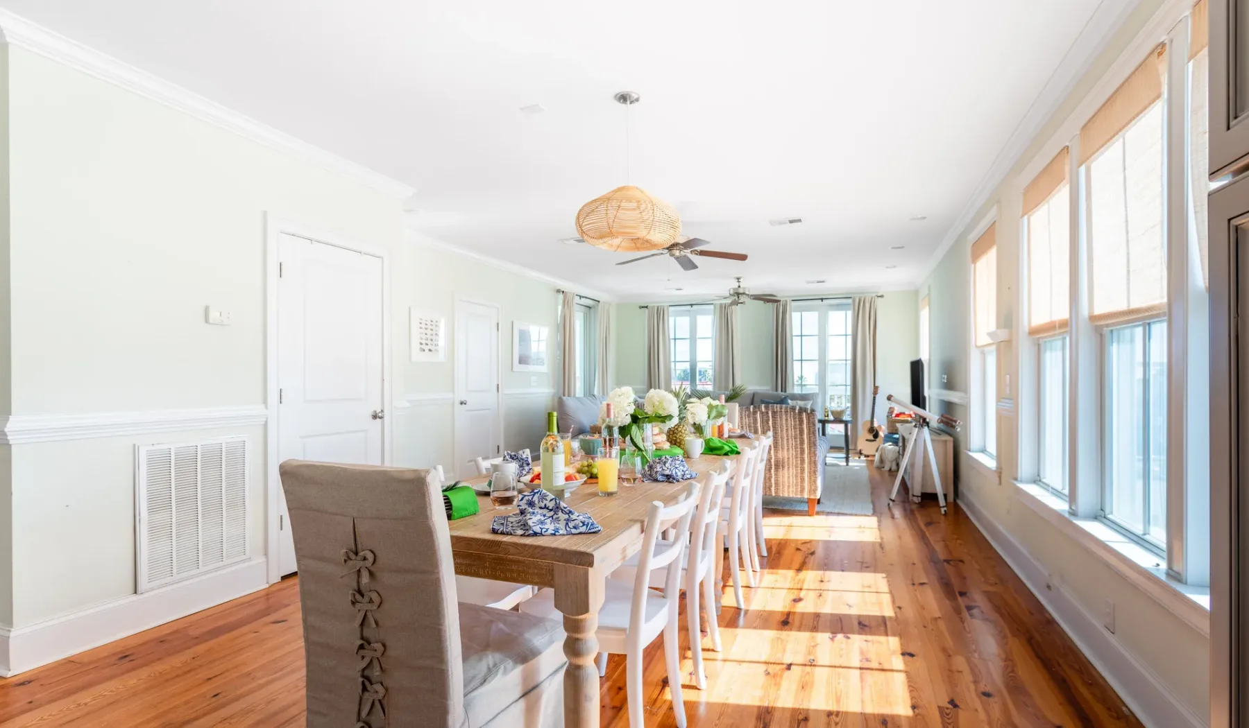A bright dining room with a long table beside large windows.