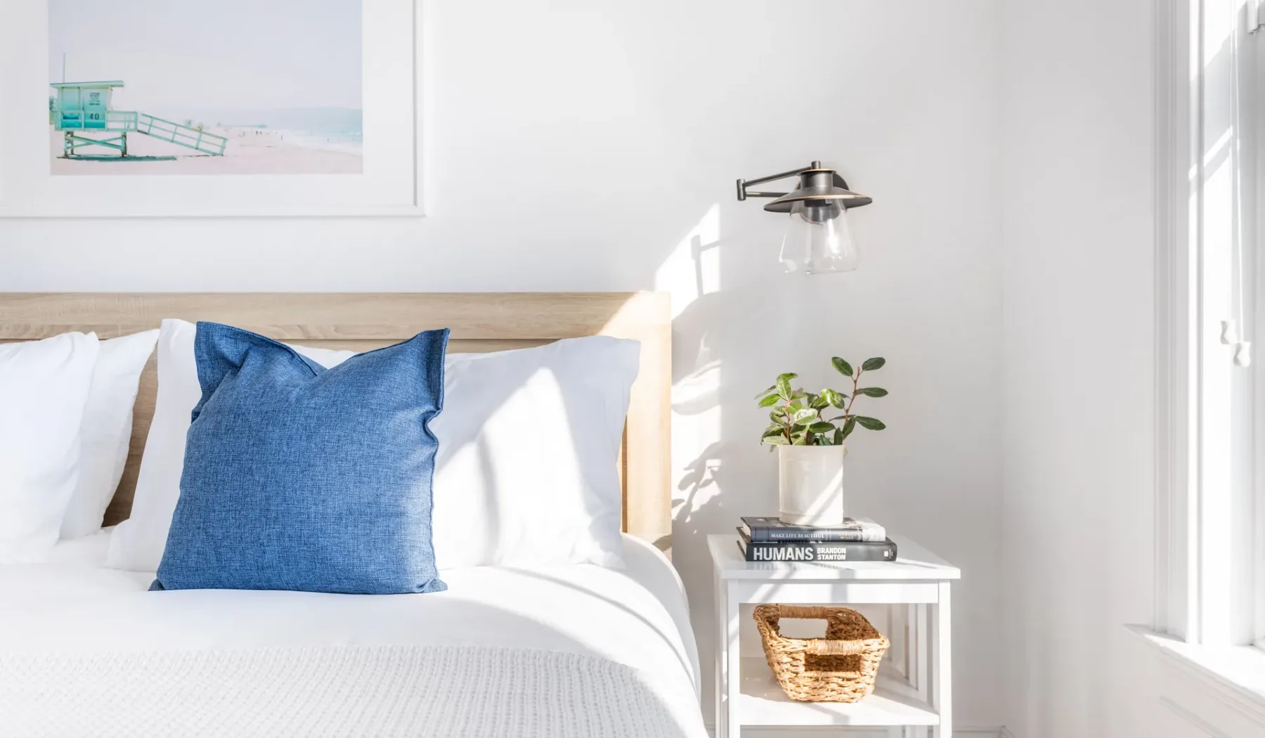 A bright bedroom with a bed, blue pillow, and small bedside table.