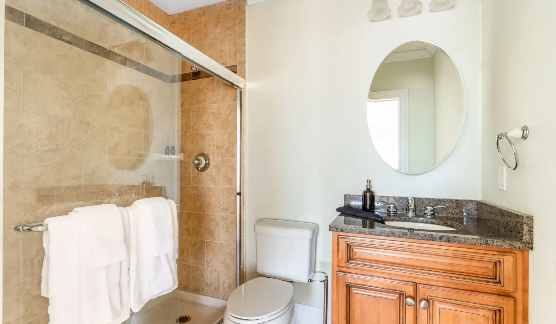 A bathroom with a glass shower, toilet, and wooden vanity.