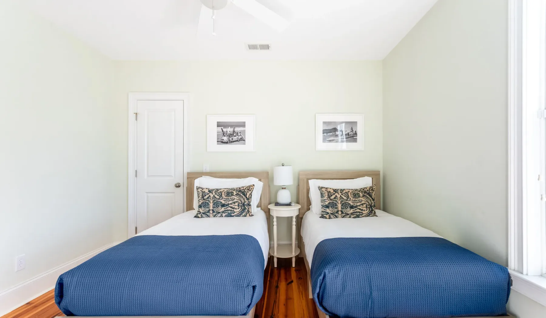 A bright bedroom with two beds dressed in blue bedding.