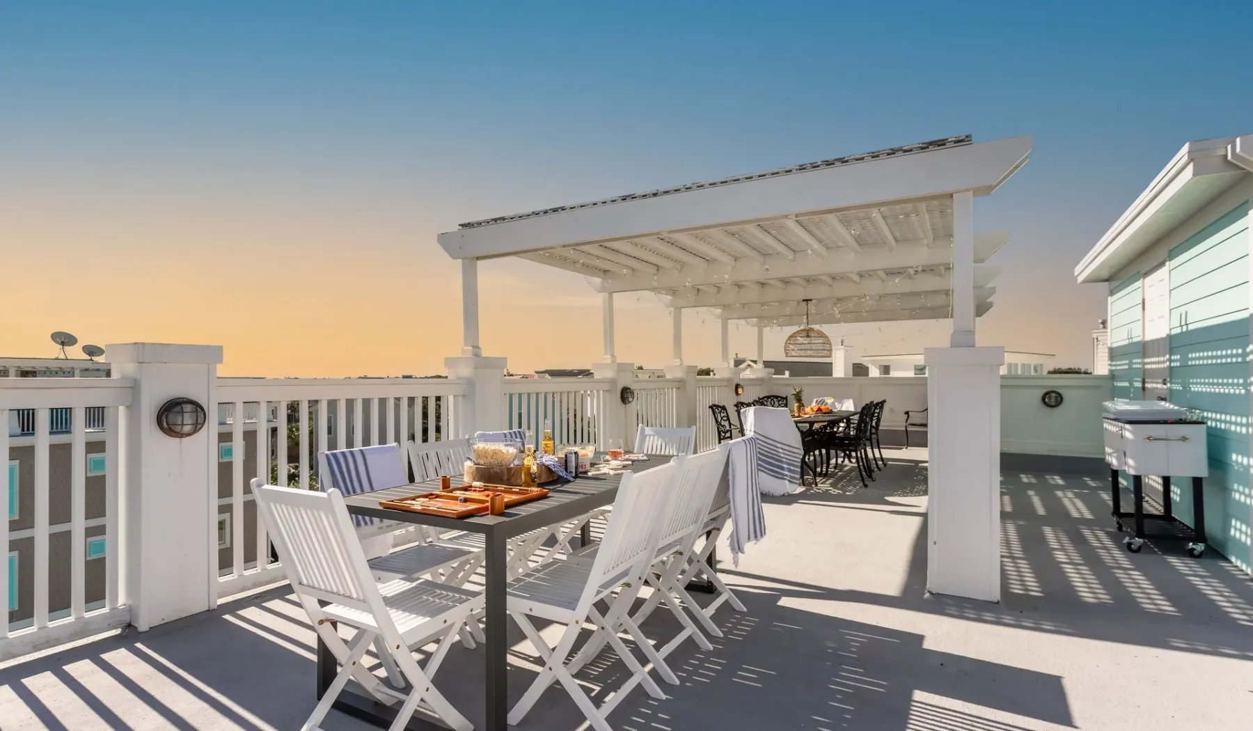 Una terraza de comedor en la azotea con asientos blancos bajo una pérgola.