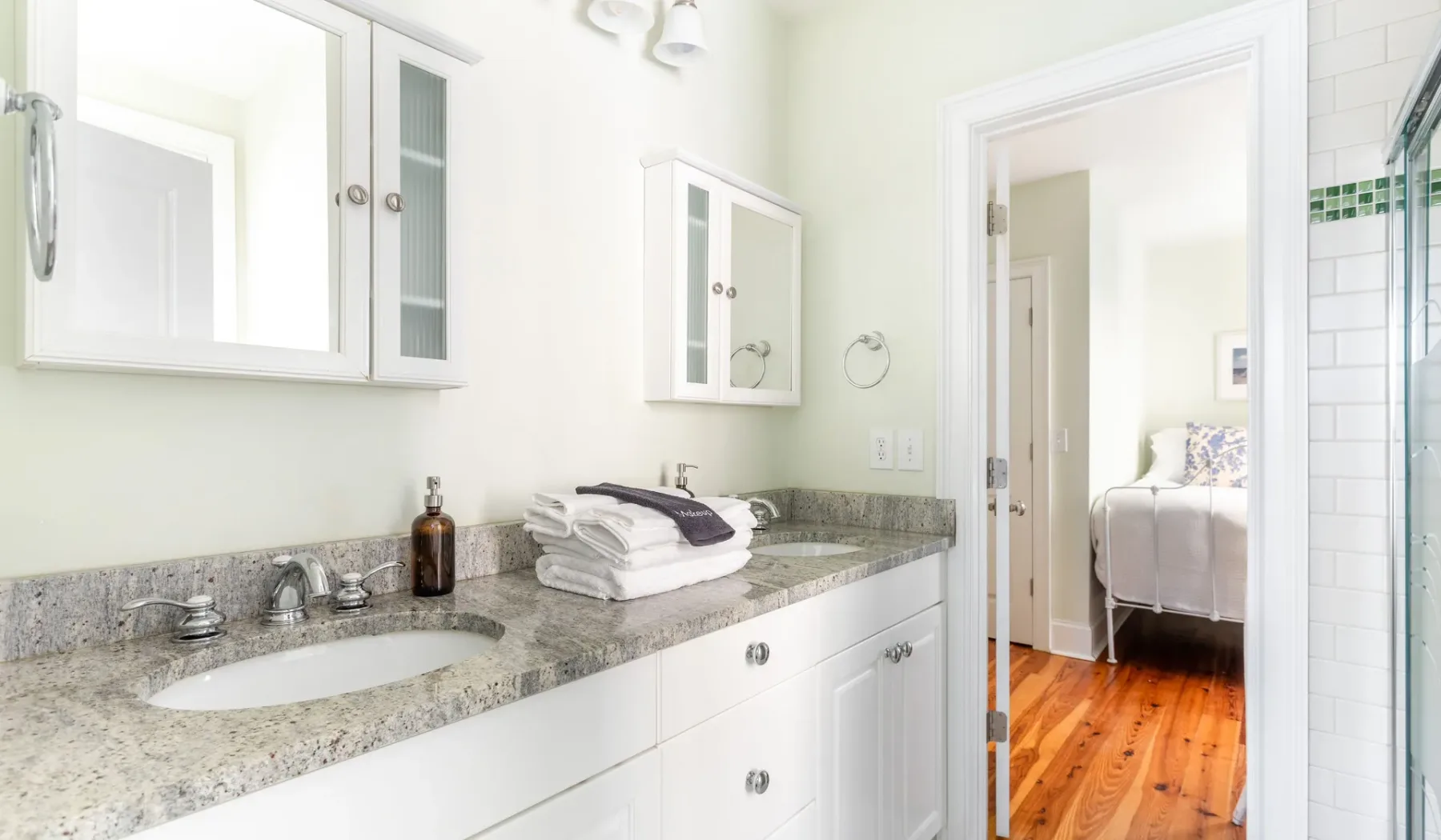 A bright bathroom with a long vanity and an open doorway to a bedroom.