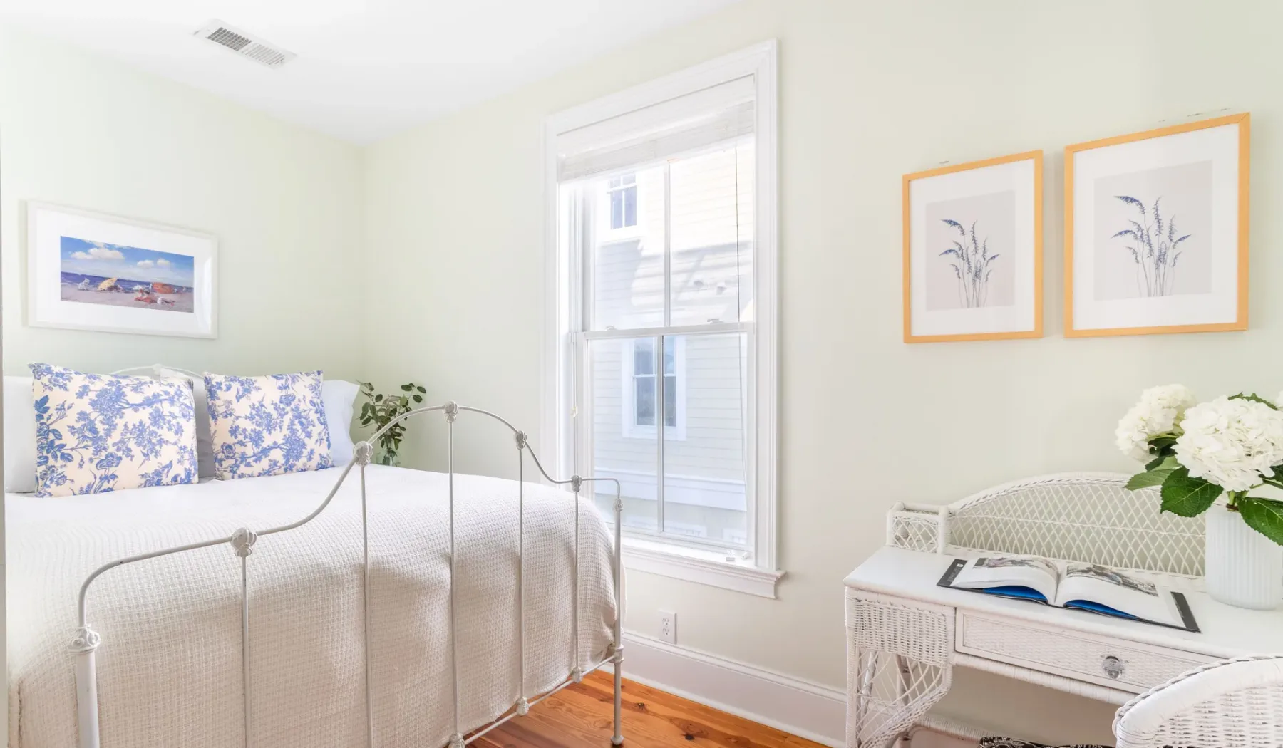 A bright bedroom with a metal bed, floral pillows, and a window.