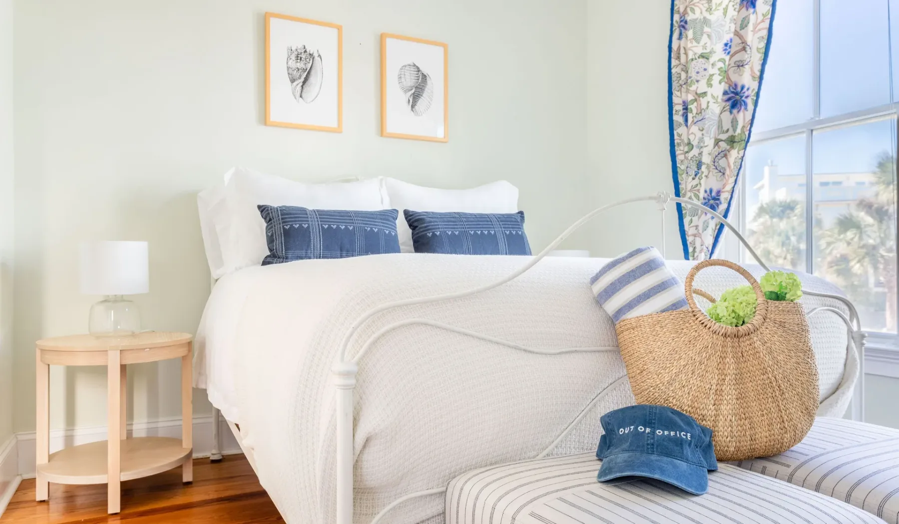 A bright bedroom with white bedding, blue accents, and a large window.