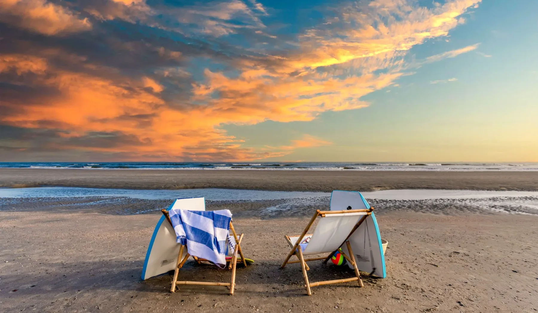 Beach scene at sunset, with two folding chairs facing the ocean.