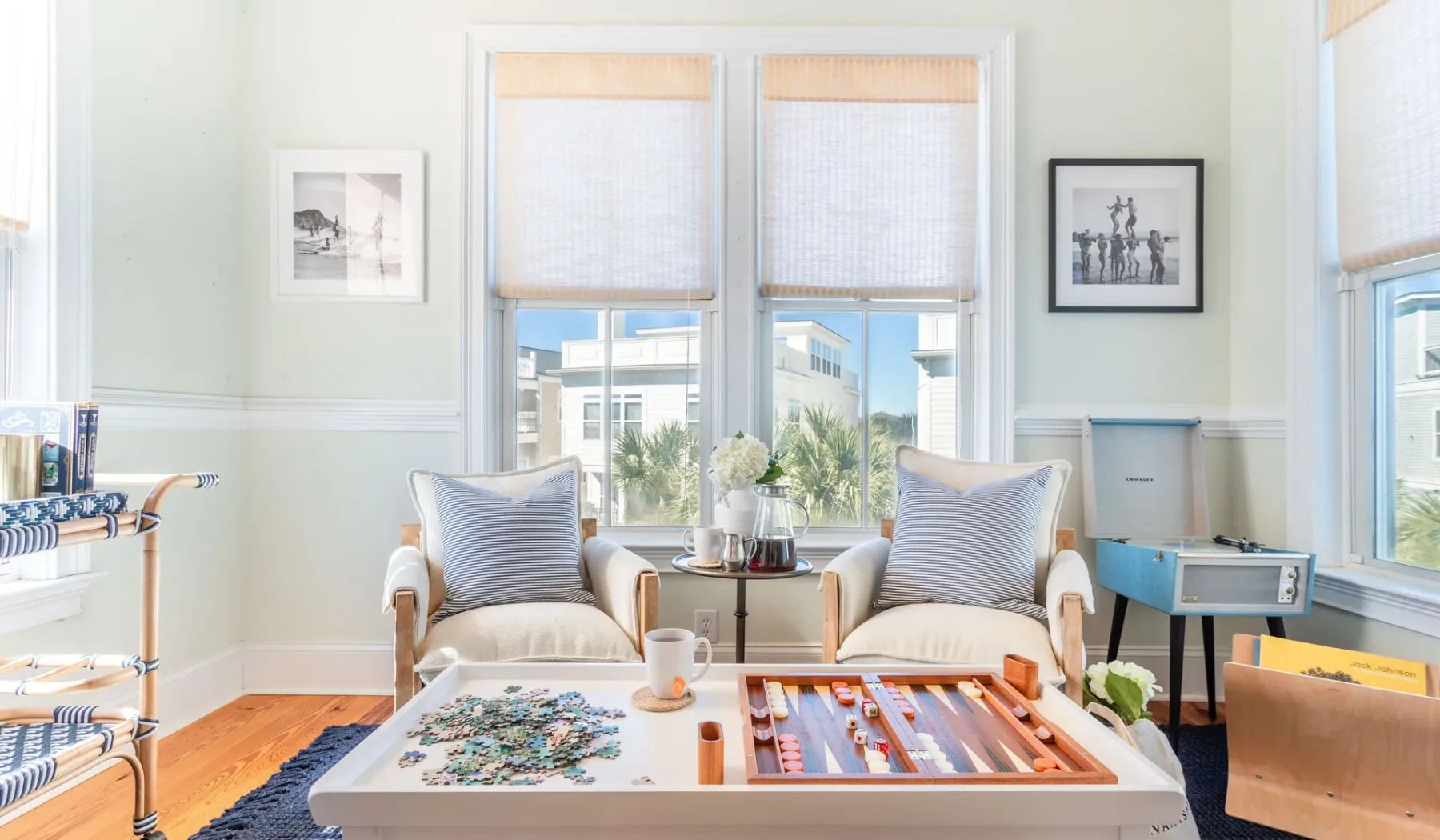 A bright sitting room has two armchairs beside tall windows and a low table.