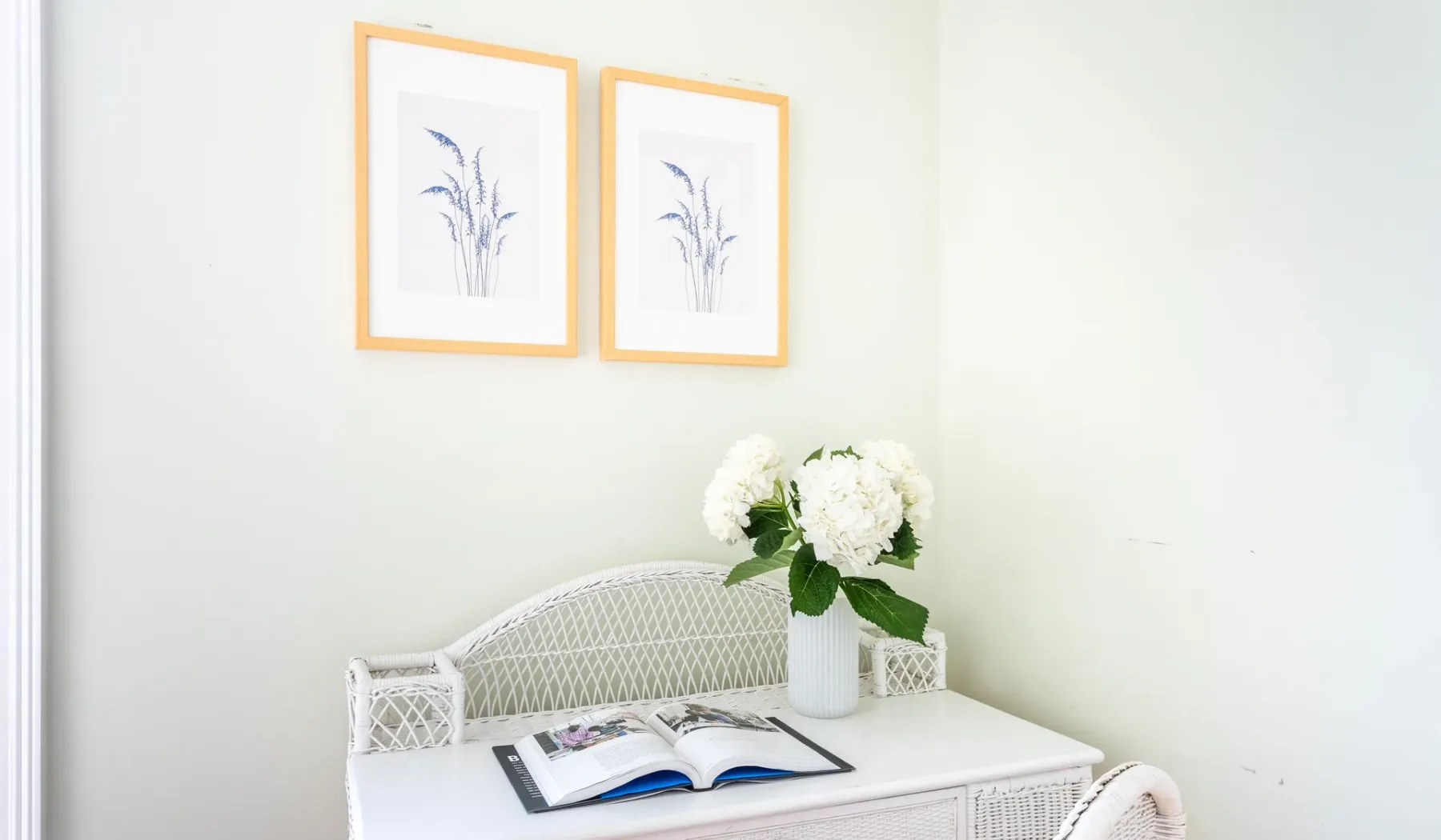 A bright sitting area has framed botanical prints and an open book on a white table.