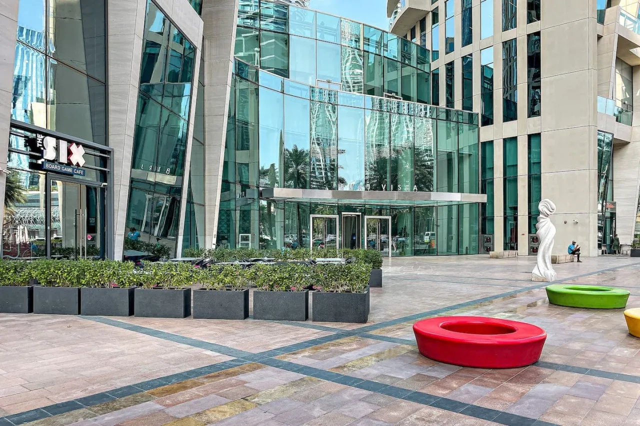 Un edificio moderno con fachada de vidrio da a una plaza pavimentada con asientos circulares de colores.