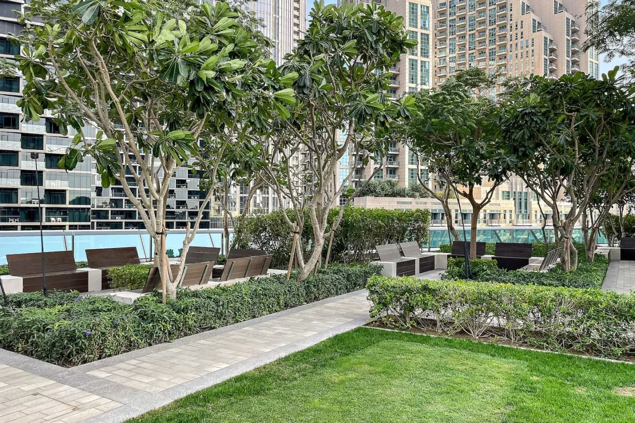 Un patio ajardinado con senderos pavimentados, césped, árboles y asientos.