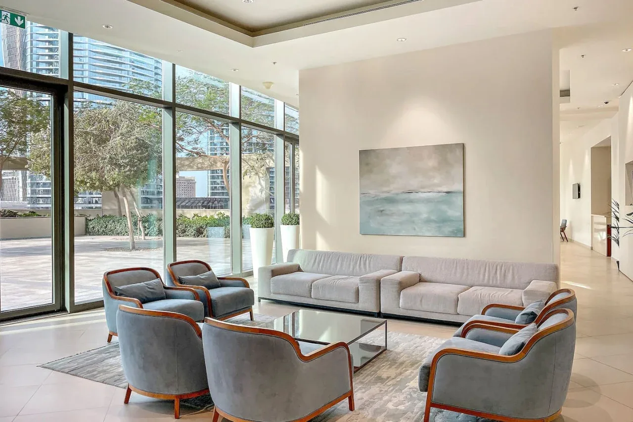 Una sala luminosa con grandes ventanales, asientos y una pintura de paisaje.