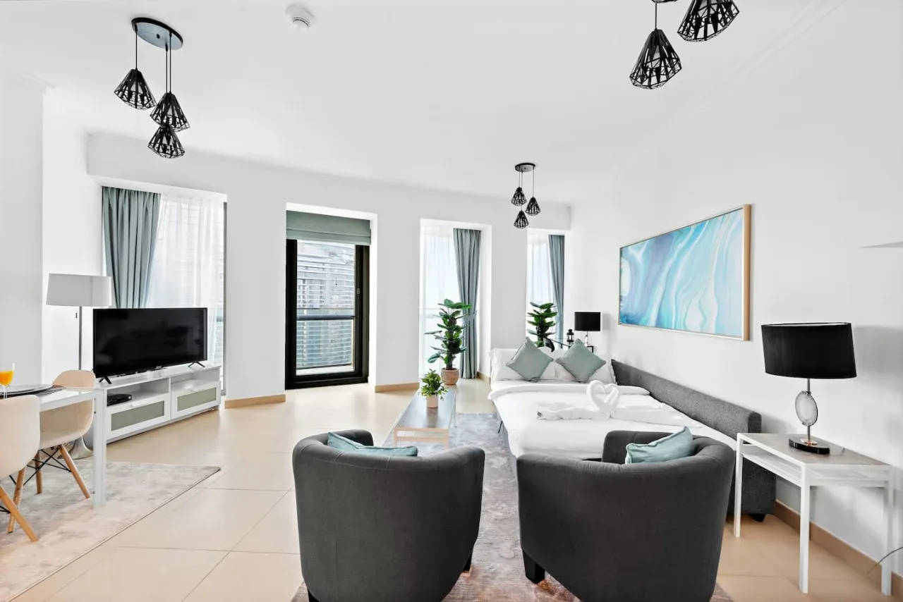 Una sala luminosa con asientos, un televisor y ventanas grandes.