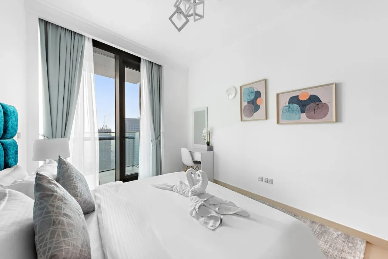 Un dormitorio luminoso con una cama junto a puertas de vidrio altas que dan a un balcón.
