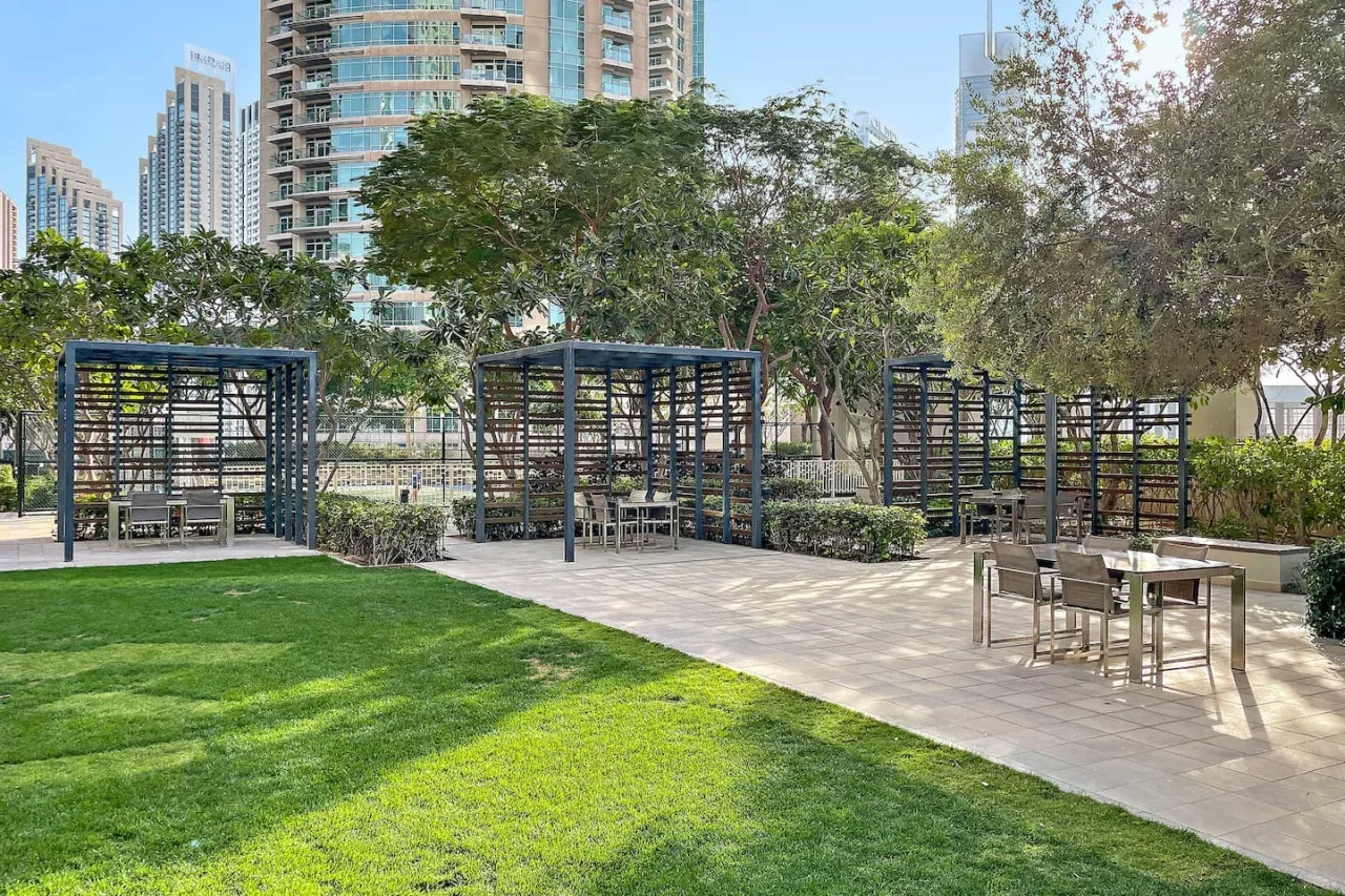 Zona ajardinada al aire libre con pérgolas, mesas y césped verde.
