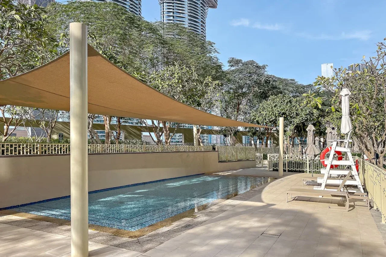 Una piscina al aire libre está bajo una vela de sombra, con tumbonas cerca.