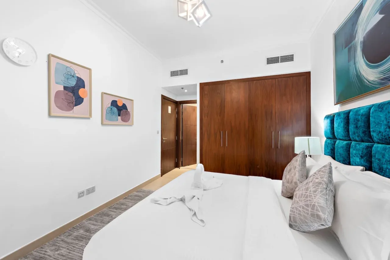 Dormitorio con cama blanca, armario de madera y cabecero tapizado en color turquesa.