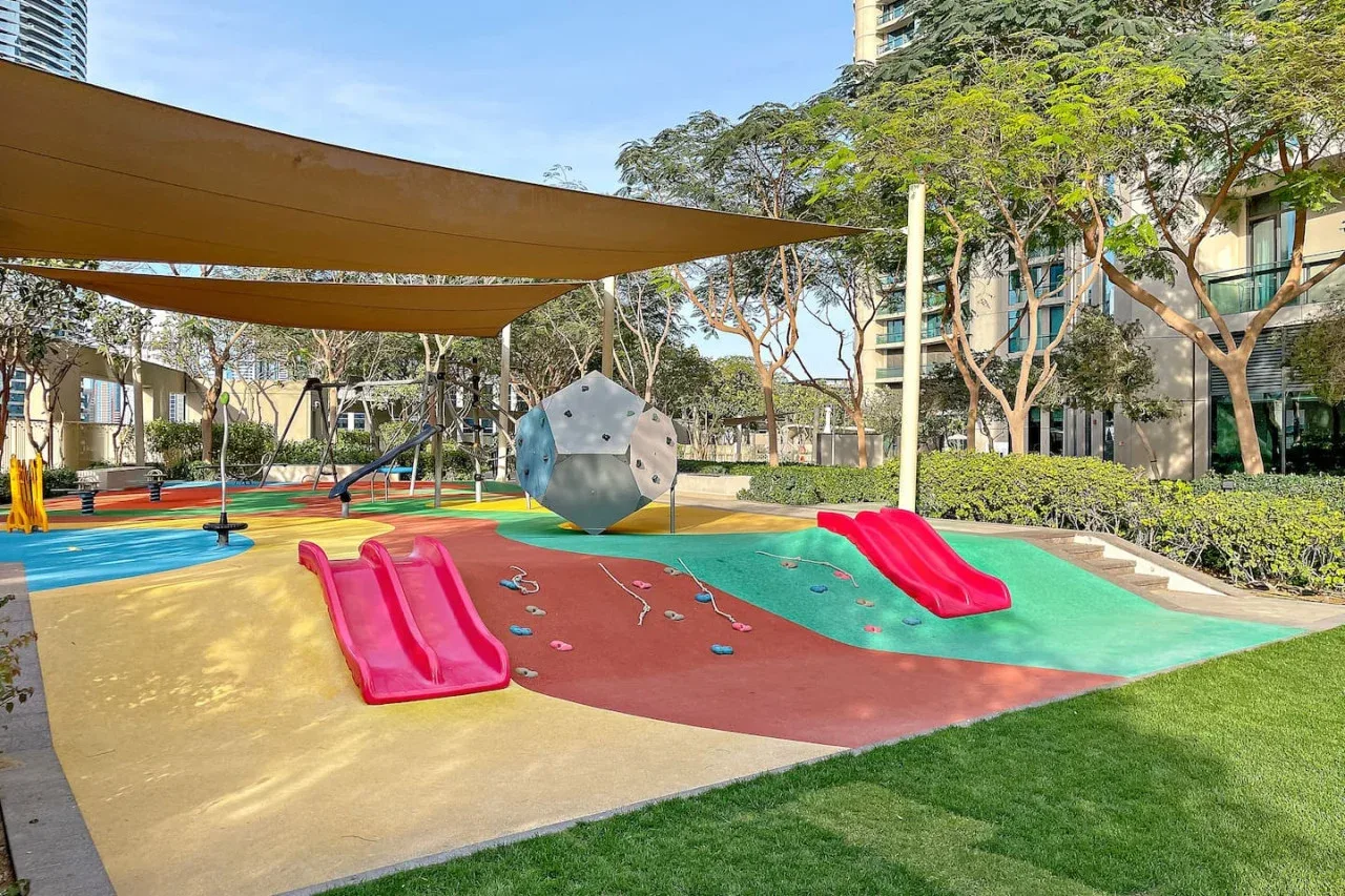 Un parque infantil al aire libre y a la sombra tiene toboganes de colores y una estructura para trepar.