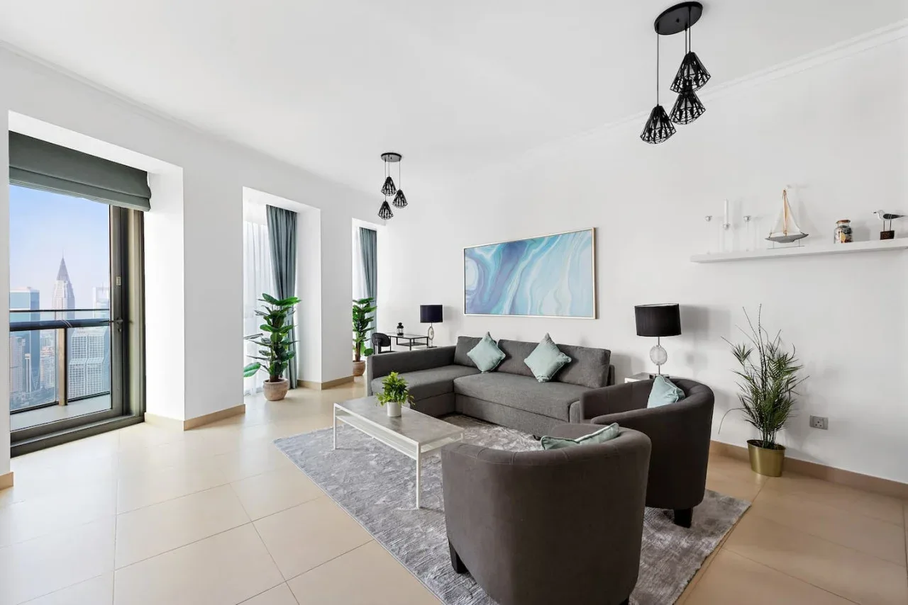 Una sala luminosa con asientos grises, una mesa de centro de vidrio y grandes ventanas.