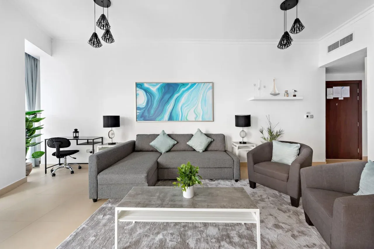 Una sala de estar luminosa con asientos grises, una mesa de centro y arte abstracto azul en la pared.